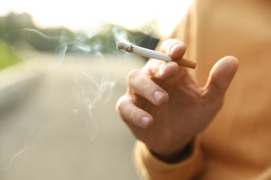 Man with cigarette outdoors, closeup of hand. Space for text