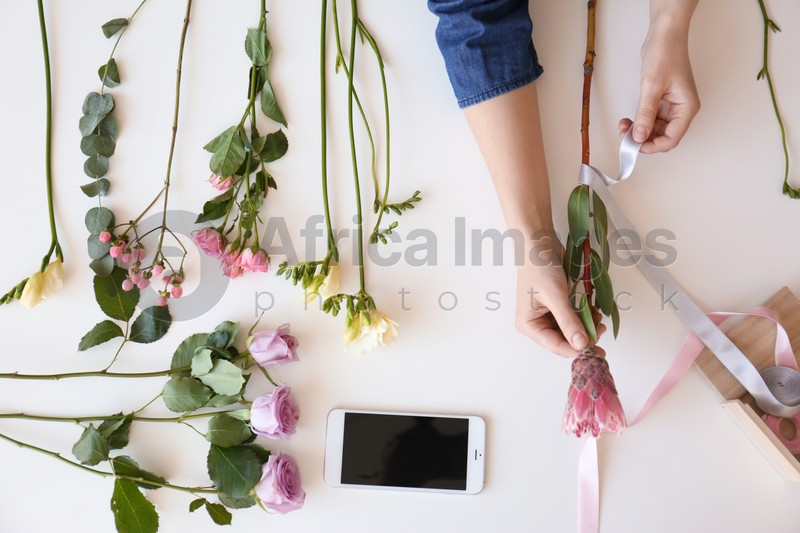 Female florist creating beautiful bouquet at table, top view