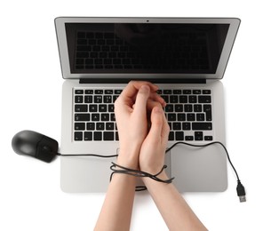 Woman showing hands tied with computer mouse cable near laptop on white background, top view. Internet addiction