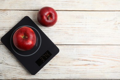 Ripe red apples and electronic scales on white wooden table, flat lay. Space for text