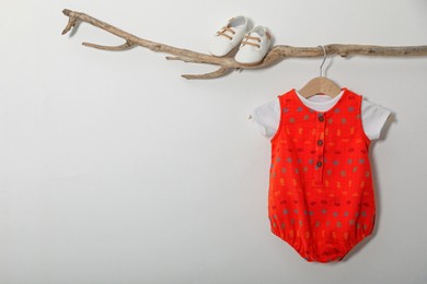 Baby bodysuit and booties on decorative branch near light grey wall. Space for text