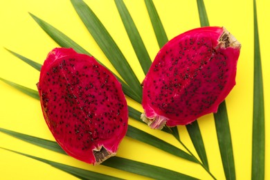 Delicious cut red pitahaya fruit with palm leaf on yellow background, flat lay