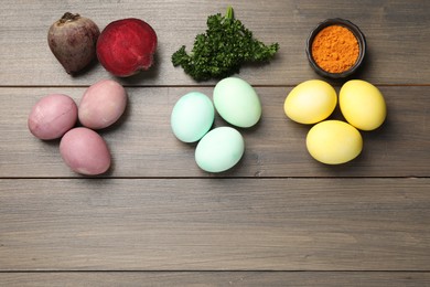 Photo of Colorful Easter eggs painted with natural dyes and ingredients on wooden table, flat lay. Space for text