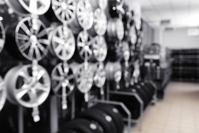 Blurred view of car tires and alloy wheels on rack in auto store