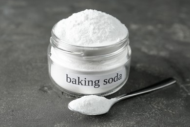 Jar and spoon with baking soda on grey table, closeup