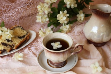Cup of aromatic tea, tasty dessert and beautiful jasmine flowers on pink fabric