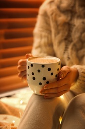 Woman with cup of hot drink at home, closeup