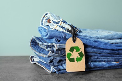 Stack of jeans with recycling label on grey table 
