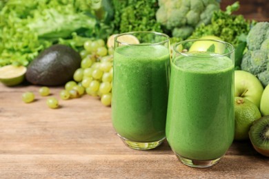 Glasses of fresh green smoothie and ingredients on wooden table, space for text