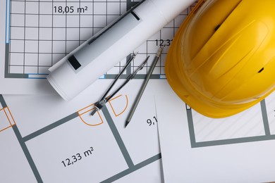Rolled construction drawing, safety hat, pair of compasses and pencil on house plan, flat lay