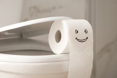 Photo of Roll of paper with funny face on toilet bowl in bathroom, closeup