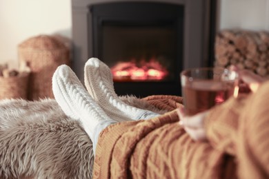 Woman with cup of tea resting near fireplace at home, closeup