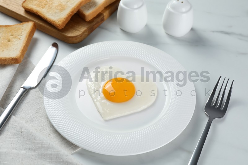 Romantic breakfast with heart shaped fried egg served on white marble table