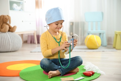 Cute child imagining himself as doctor while playing with stethoscope and toy bear at home