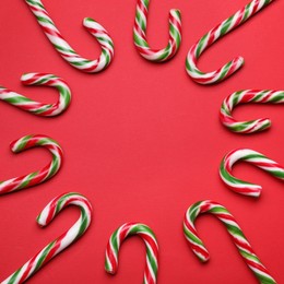 Many sweet Christmas candy canes on red background, flat lay. Space for text