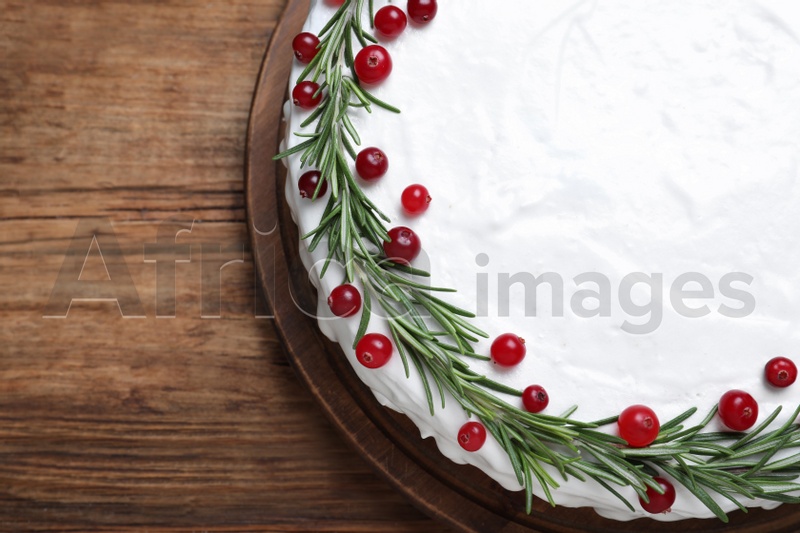 Photo of Traditional Christmas cake decorated with rosemary and cranberries on wooden table, top view