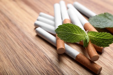 Menthol cigarettes and mint leaves on wooden table, closeup. Space for text