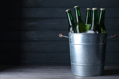 Photo of Metal bucket with bottles of beer and ice cubes on wooden table against dark background, space for text