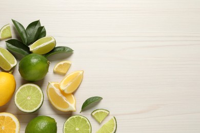 Fresh ripe lemons, limes and green leaves on white wooden background, flat lay. Space for text