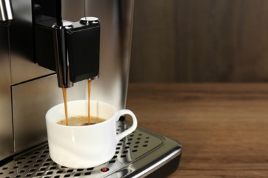 Modern espresso machine pouring coffee into cup on wooden table, closeup. Space for text