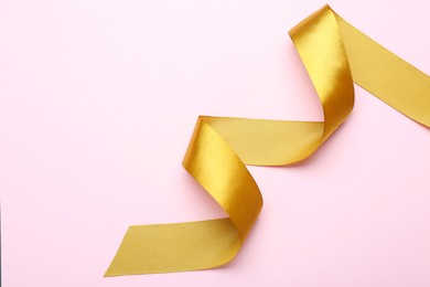 Beautiful golden ribbon on pink background, top view. Space for text