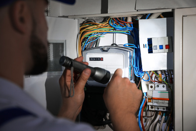 Electrician with flashlight fixing electric panel indoors