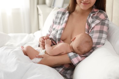 Photo of Young woman breastfeeding her little baby on bed at home, closeup