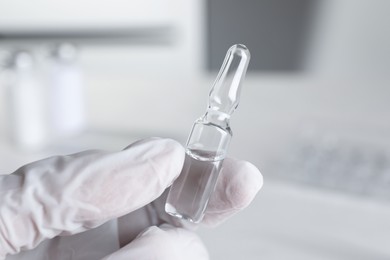 Doctor holding pharmaceutical ampoule with medication indoors, closeup