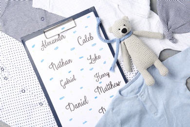 Clipboard with different baby names and toy on child's clothes, top view