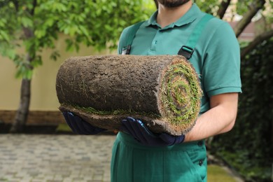 Photo of Worker holding rolled grass sod at backyard, closeup