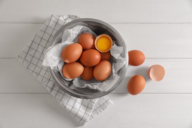 Photo of Fresh raw chicken eggs with bowl and napkin on white wooden table, flat lay