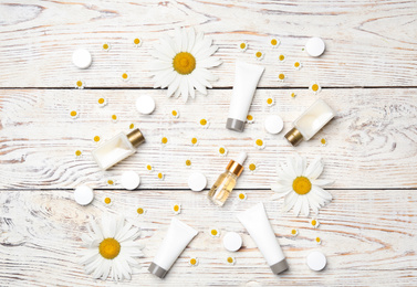 Flat lay composition with chamomile flowers and cosmetic products on white wooden table