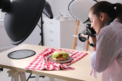 Young woman with professional camera taking photo of sandwich in studio. Food photography