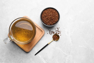 Cup of aromatic buckwheat tea and granules on light marble table, flat lay. Space for text