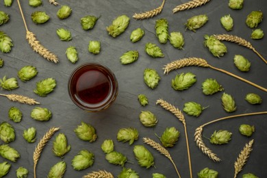 Photo of Glass of beer, fresh green hops and spikes on dark grey table, flat lay