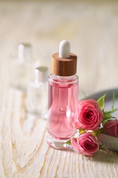 Bottle of essential rose oil and flowers on white wooden table