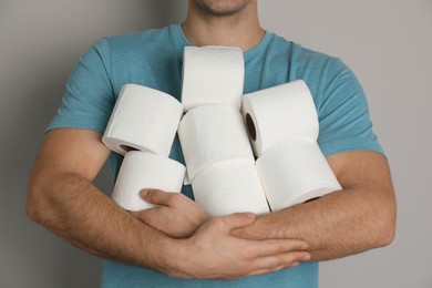 Man with heap of toilet paper rolls on grey background, closeup