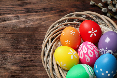 Colorful Easter eggs in decorative nest on wooden background, closeup. Space for text