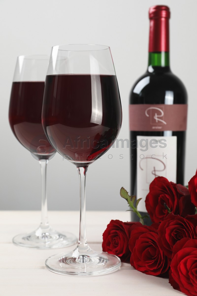 Photo of Bottle and glasses of red wine near beautiful roses on white wooden table