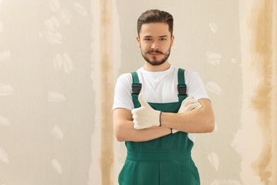 Photo of Happy worker in uniform near wall with putty indoors. Space for text