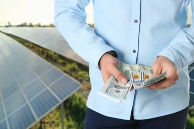 Man with money and installed solar panels on background, closeup. Economic benefits of renewable energy