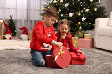 Cute little children with gift boxes near Christmas tree at home