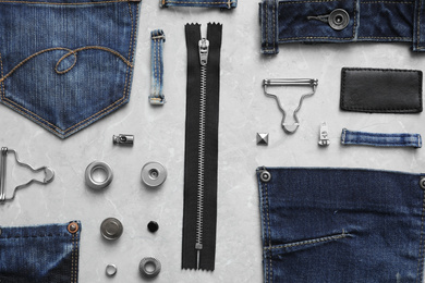 Flat lay composition with garment accessories and cutting details for jeans on grey marble background