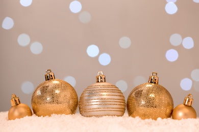 Beautiful golden Christmas balls on snow against blurred festive lights. Space for text