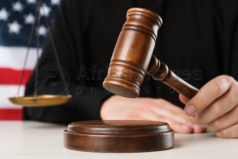 Photo of Judge with gavel at white wooden table near flag of United States, closeup