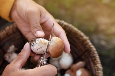 Man peeling mushroom with knife over basket outdoors, closeup