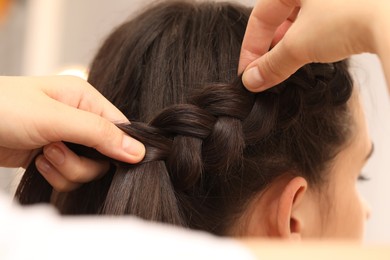Professional stylist braiding client's hair on blurred background, closeup