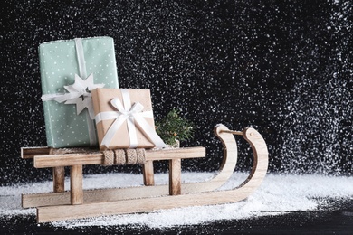 Sleigh with gift boxes on black wooden table during snowfall