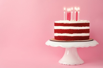 Delicious homemade red velvet cake with candles on pink background. Space for text