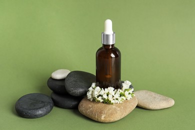 Composition with bottle of face serum, spa stones and beautiful flowers on light green background